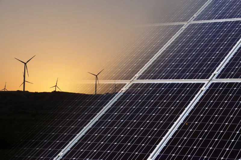 Solarpanele im Vordergrund, Windraeder im Sonnenuntergang — Symbolbild fuer erneuerbare Energien als Schutz vor Energiekrisen
