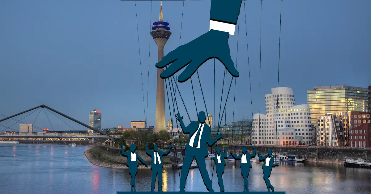 Marionetten-Hand steuert Figuren vor Düsseldorfer Skyline