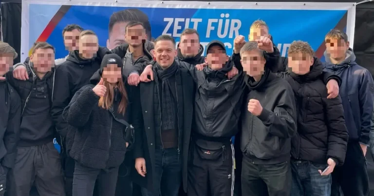 Hannes Gnauck (AfD) posiert grinsend mit einer Gruppe schwarz gekleideter Jugendlicher vor einem AfD-Wahlkampfbanner in Templin