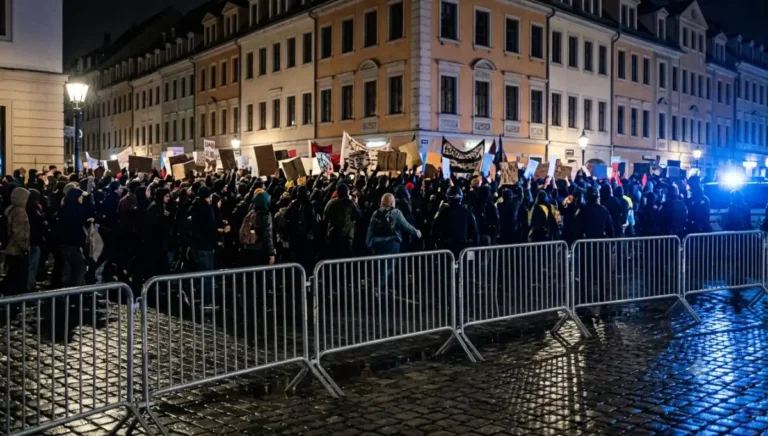 Demonstrationszug bei Nacht hinter Absperrgittern auf Kopfsteinpflaster, Blaulicht, europäische Stadtarchitektur – Symbol für Gegenproteste beim AfD-Parteitag Erfurt 2026