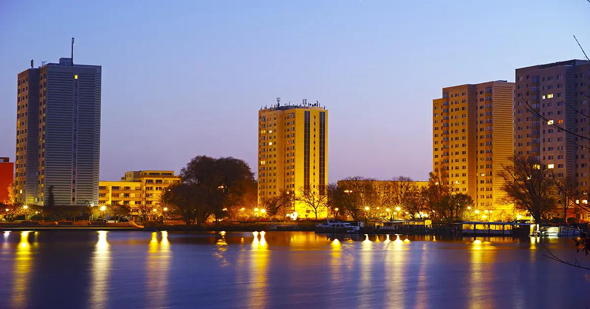 Plattenbau-Hochhäuser in Potsdam spiegeln sich im Abenddunkel in der Havel, warme Straßenbeleuchtung